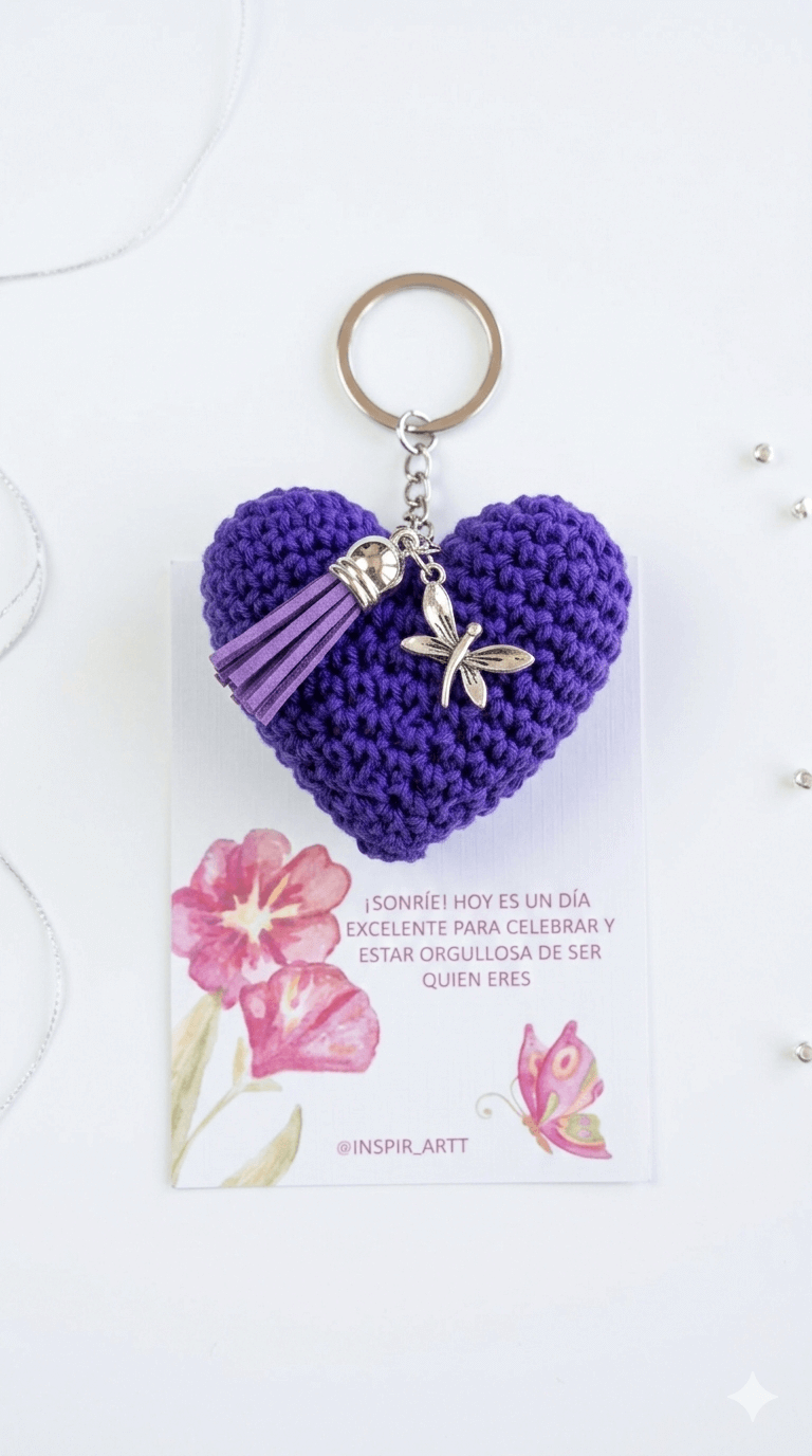 Llavero de corazón tejido a crochet en color morado con borla de flecos y dije metálico de libélula sobre fondo blanco.