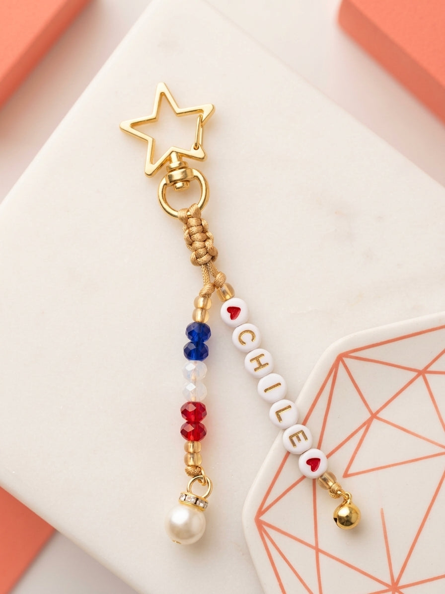 Llavero dorado con mosquetón en forma de estrella, cuentas con la palabra Chile entre corazones, cristales en azul, blanco y rojo.