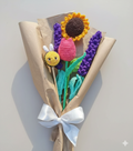 Ramo de flores tejidas a crochet envuelto en papel café con un lazo, que incluye un girasol, un tulipán, lavandas y una pequeña abejita amigurumi.