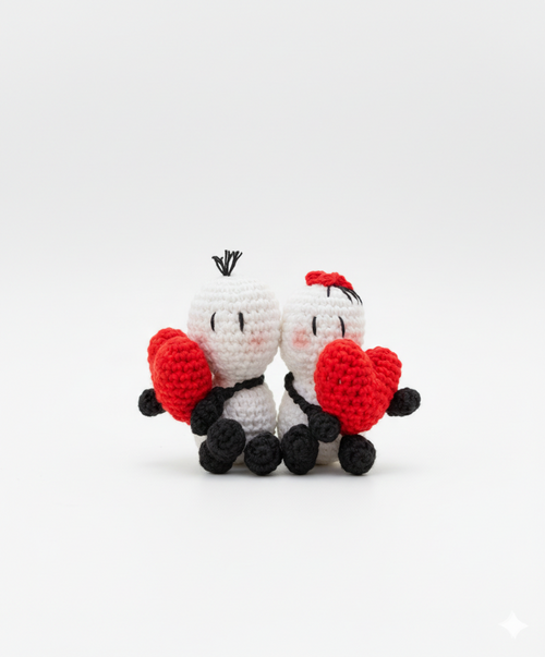 Pareja de amigurumis blancos Bigli y Migli con corazones rojos tejidos a mano sobre fondo de madera.