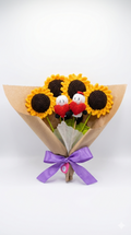Ramo de 4 girasoles tejidos a crochet y una pareja de personajes Bigli y Migli con corazones rojos, envuelto en papel café con un lazo morado.