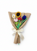 Ramo de flores tejidas a crochet envuelto en papel café que incluye una cala, una rosa, un girasol, un tulipán y un corazón.