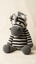Muñeca cebra tejida a mano en técnica amigurumi con rayas blancas y negras, sentada sobre un fondo neutro.