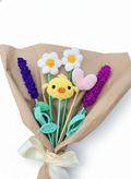 Ramo de flores tejidas a mano que incluye un pollito amarillo amigurumi, margaritas blancas, lavandas púrpuras y un corazón rosado, envuelto en papel café.